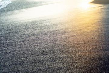 Beach with black volcanic sand and reflection of the sun at sunset