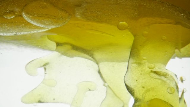 Close-up view of golden liquid stirred by teaspoon. Liquid yellow wave line. Close shot of pouring sesame oil and golden black cumin oil on white background. Water does not mix with water in a tank.