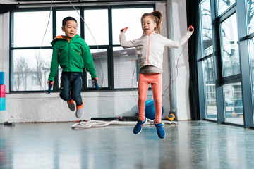 Front view of multicultural children doing exercise with jump rope in gym