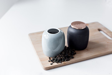 two teapots stand on a wooden board on a white table in a bright kitchen, next to which green tea is scattered