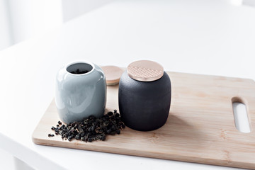 two teapots stand on a wooden board on a white table in a bright kitchen, next to which green tea...