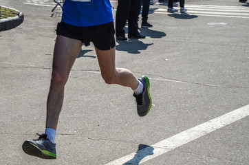 Legs of runner while he runs at marathon race in the city. Muscular legs of the athlete runner from...