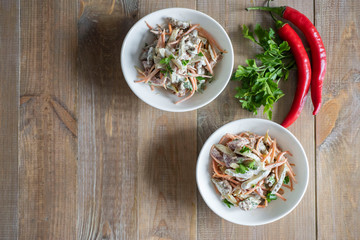 Meat salad with vegetables and mayonnaise in white salad bowls on a wooden table