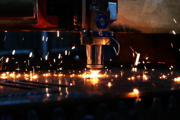 The laser machine cuts a metal sheet and bright sparks fly out of its work. Laser machine at a metalworking factory. - obrazy, fototapety, plakaty