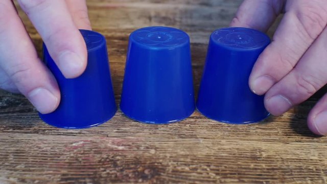 thimblerig.a hidden pea under one of the glasses moves them around the table