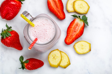 Smoothie or milkshake cocktail made from fresh strawberries, banana, yogurt or milk and ice cubes in Mason jar on a marble table. Concept of healthy vitamin drinks. Selective focus, top view