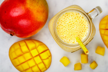 Smoothie or milkshake made from fresh  mango, yogurt or milk and ice cubes in Mason jar on a marble table. Concept of healthy vitamin drinks. Selective focus, top view - 324005077