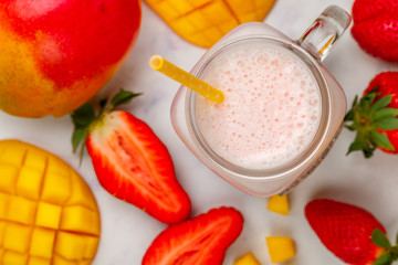 Smoothie or milkshake made from fresh strawberries, mango, yogurt or milk and ice cubes in Mason jar on a marble table. Concept of healthy vitamin drinks. Selective focus, top view