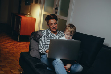 mid aged woman with her son relaxed on sofa using laptop at her home