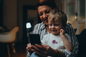 mid aged woman with her son relaxed on sofa using mobile phone at her home