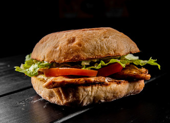 italian ciabatta panini sandwich with chicken, cheese and tomato on black wooden table