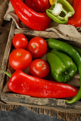 Red tomatoes and green peppers in a wooden container.