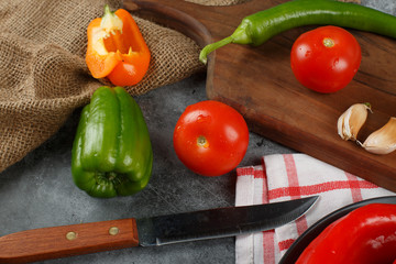 Peppers, tomato and garlics with a knife on a wooden board.
