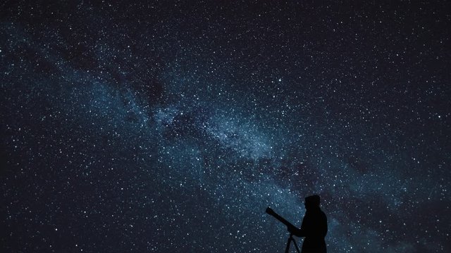 a silhouette of the astronomer with telescope observing night sky. Girl standing with telescope on the background of the starry sky. Time lapse of the moving Milky Way. 