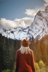 Attractive blonde girl in a red knitted hat stands with her back to the camera on a background of...
