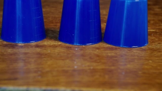 thimblerig.a hidden pea under one of the glasses moves them around the table