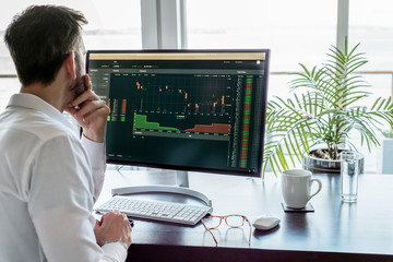 Man researching exchange market data on modern computer screen, desk with keyboard, mouse,...