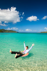 Excited office worker throwing his arms and legs up in celebration floating outdoors in a tropical island sea with his laptop computer