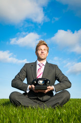 Calm office worker meditating in bright green meadow holding an old-fashioned rotary dial telephone