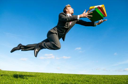 Careless office worker tripping dramatically with his file folders flying outdoors in a green grass field