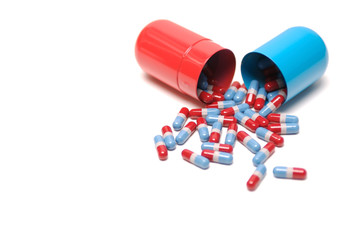 Big pile of red, white, and blue medicine pills spilling out of a bigger red and blue capsule canister on white background