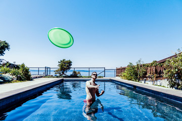 Man throwing a green flying disc from swimming pool under blue sky.