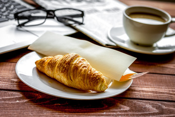 Business lunch with croissant and laptop on wooden desk