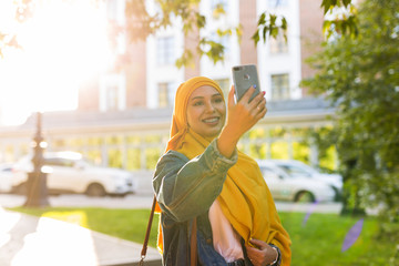 Muslim girl in hijab makes a selfie on the phone standing on the street of the city