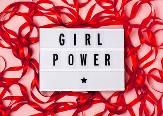 Girl power inscription on the lightbox, red ribbon on the pink background. 8 march, women's day, feminism concept. Top view, flat lay composition