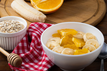 Bowl of oatmeal porridge with banana and orange  on wooden background, copy space