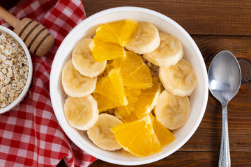 Bowl of oatmeal porridge with banana and orange  on wooden background. Top view, copy space