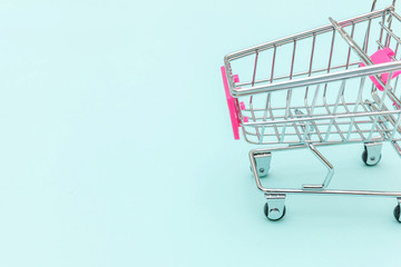 Small supermarket grocery push cart for shopping toy with wheels isolated on blue pastel colorful trendy background Copy space. Sale buy mall market shop consumer concept.