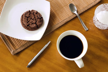 Black coffee in white cup in messy arrangement on table, chocolate cookie on white plate, teaspoon,...