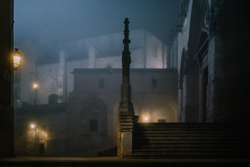 Illuminated stone fence around ancient cathedral building at dark misty night in Burgos, Spain