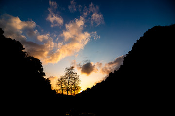 Sunset with clouds and silhouettes of trees and hills