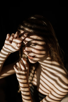 Stripe shadow from shutters falling on face of charming relaxed long haired woman smiling with closed eyes