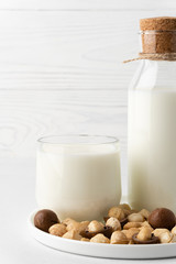 Dairy-free milk. Macadamia nut milk in a glass cup and a bottle on a flat plate, light background. Dairy products without lactose and gluten.