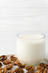 Walnut milk in a glass cup and nuts on a flat plate, white background. Dairy products without lactose. Copy space.
