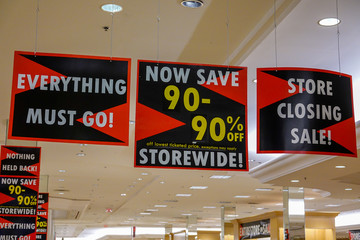 Signs for a store wide 90% off bankruptcy sale hanging from the ceiling of a store