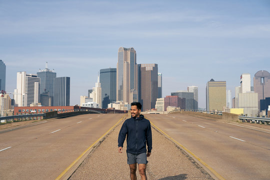 Young Hispanic male athlete in sports clothing looking away after workout standing on side of road in downtown Dallas, Texas