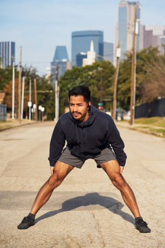 Hispanic male gymnast in active wear standing and reaching out arm to opposite foot in downtown Dallas, USA