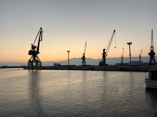 Obraz premium Silhouettes of the sea port cranes background at the sunset, natural colors