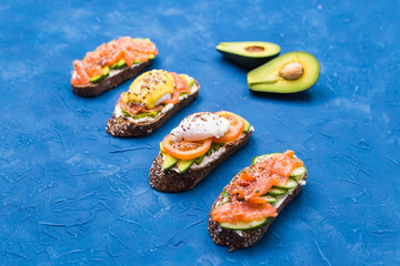 Sandwiches with smoked salmon, eggs, sauce and avocado on blue background. Concept of breakfast and healthy nutrition.