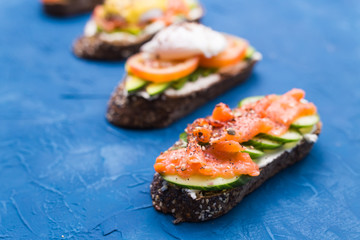 Sandwiches with smoked salmon, eggs, sauce and avocado on blue background. Concept of breakfast and healthy nutrition.