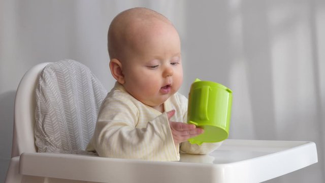 Baby Sitting In High Chair With A Green Sippy Cup.