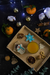 Christmas cookies in the shape of a house, a snowman and stars lie in the gap with fresh orange juice in a glass of farm-style drink. Around nuts, cinnamon, decor. Black background.