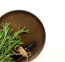 rosemary essential oil bottle and fresh rosemary leaves on wooden plate isolated on white background. copy space. flat lay, top view.