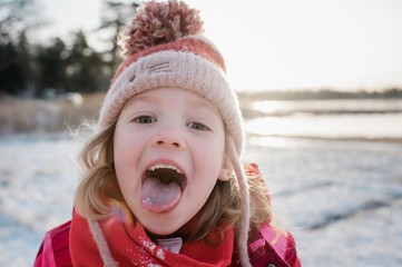 young girl catching snow on her tongue outside in winter