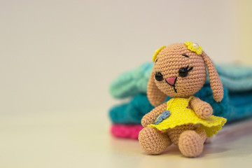 Knitted doll hare and knitted in yellow clothes - colored toy amigurumi on a light background. Copy space. needlework concept.
