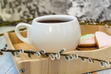 A willow twig with buds and a white cup of tea stands on a wooden tray. The concept of morning, breakfast